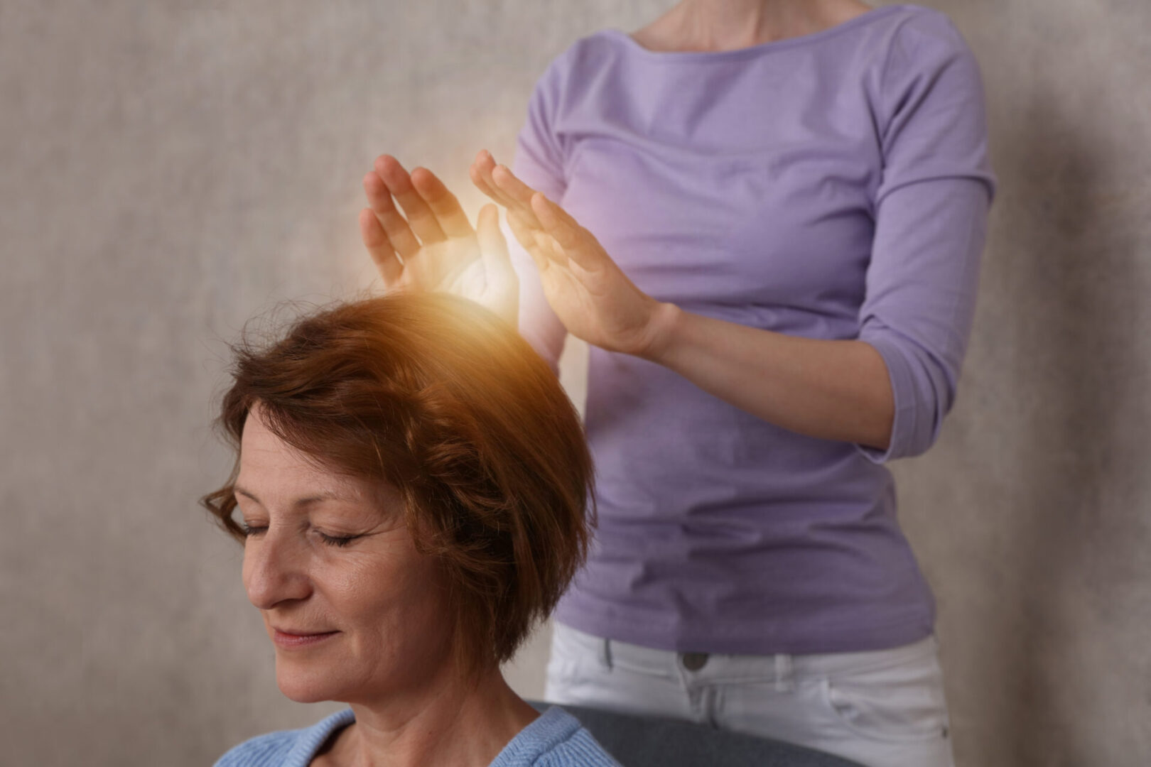 A person in a purple shirt holds hands above another person's head, emitting a warm light, suggesting an energy healing practice.