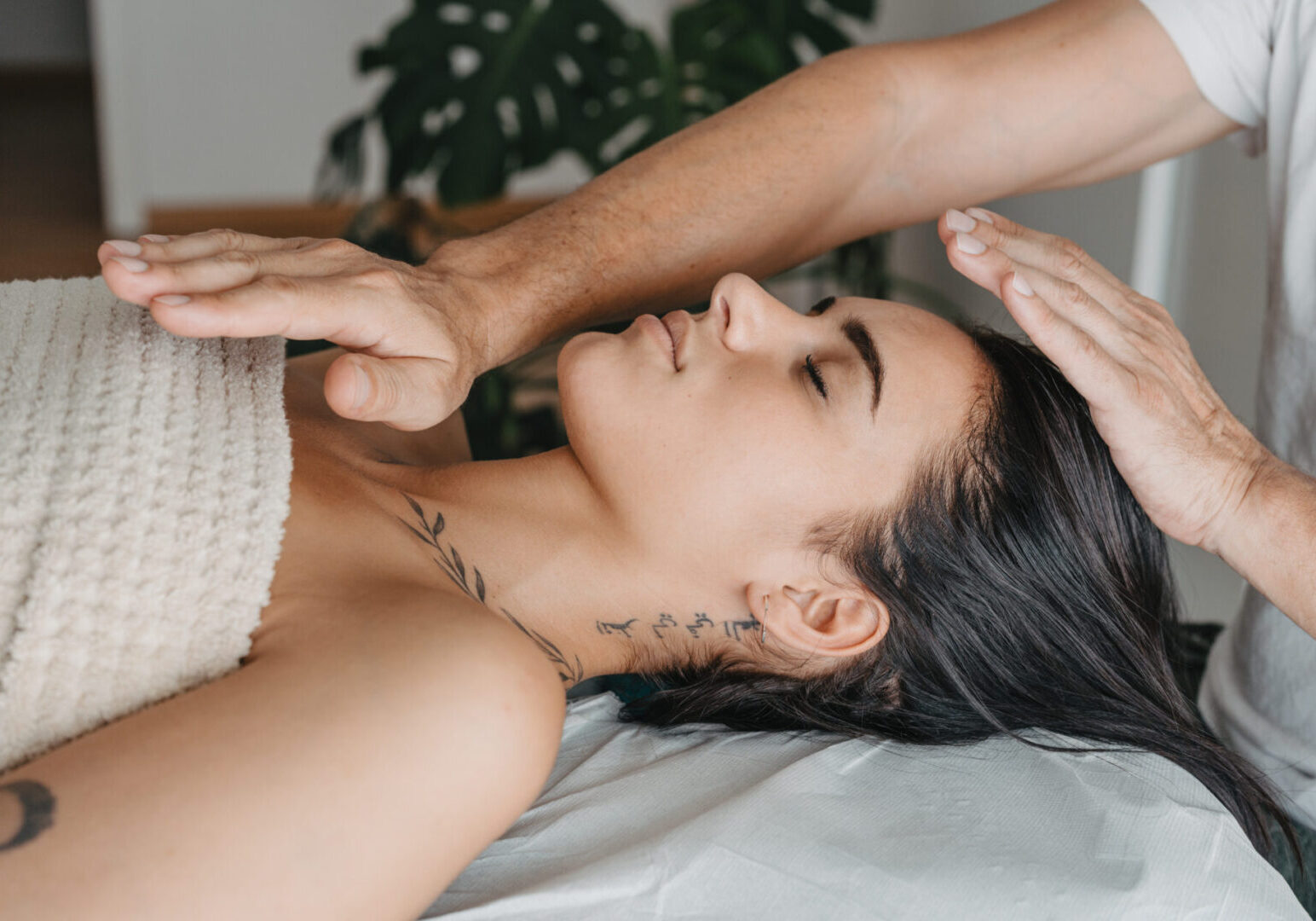 Profile of a woman while receiving energy in a Reiki therapy Person receiving reiki treatment, lying down with eyes closed, while hands hover above their head and chest.